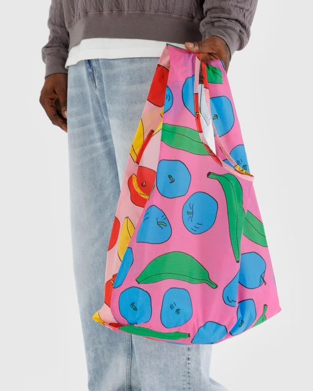 Person carrying a BAGGU reusable bag with a colorful fruit print. Shows comfortable handle length, lightweight feel, and stylish everyday use.