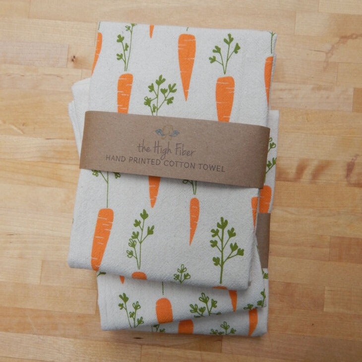 Three white hand printed organic cotton tea towels, featuring a pattern of orange carrots with green tops.