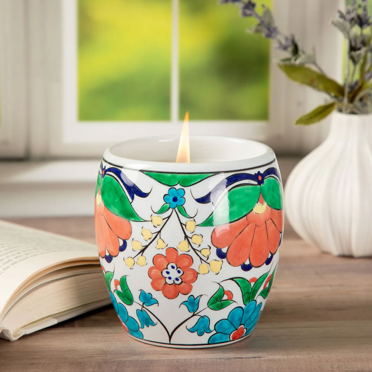 Decorative candle in a colorful ceramic holder on a table with a blurred background