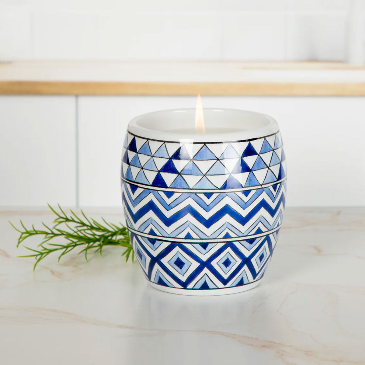 Candle in a blue and white geometric patterned container on a light wooden surface.