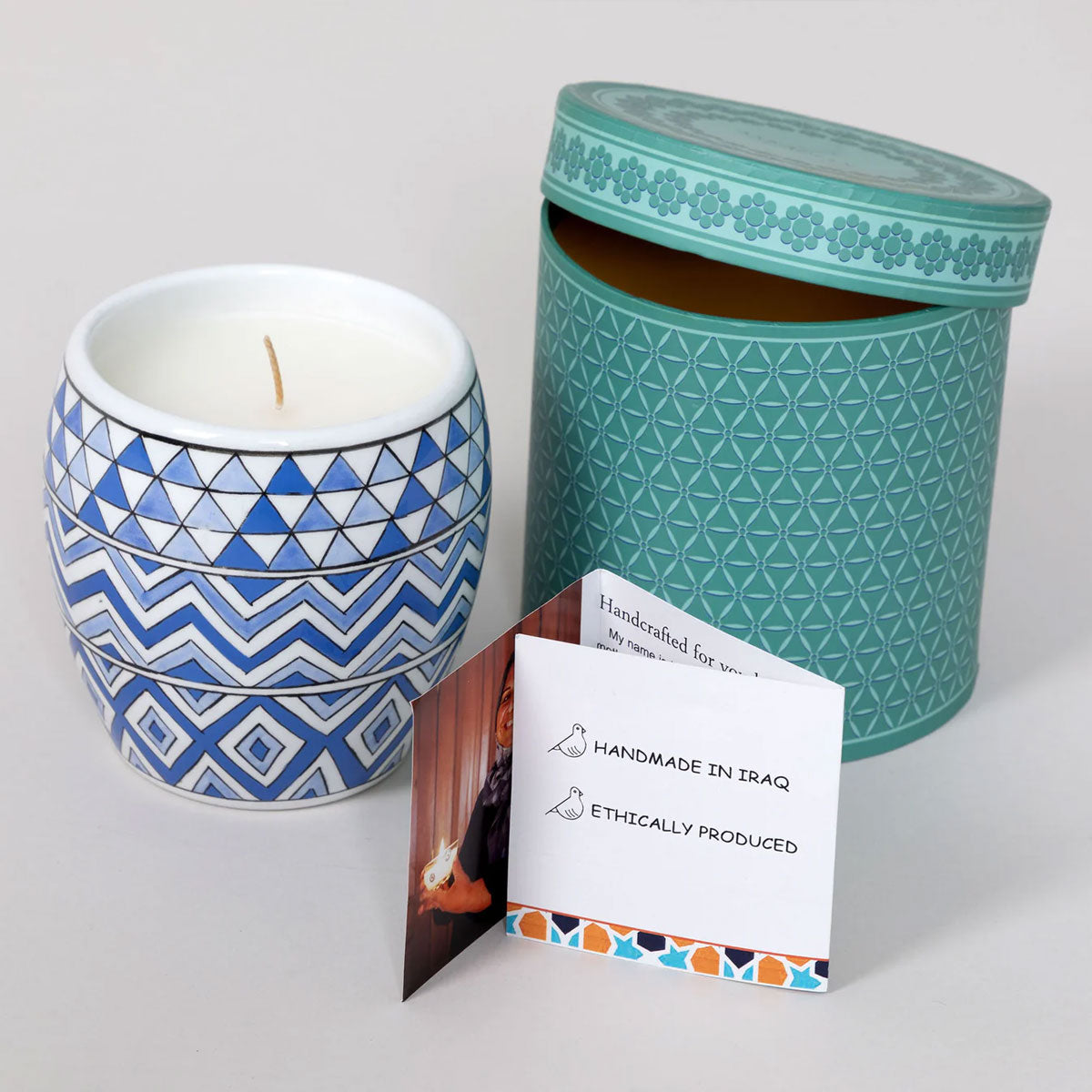 Candle with blue geometric design and teal packaging on a white background