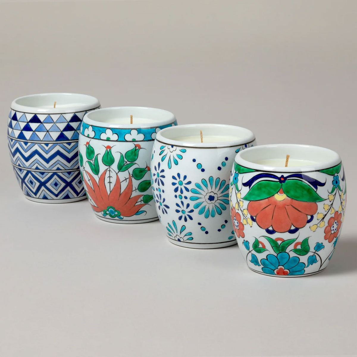 Set of four decorative candles in hand-painted ceramic holders on a light gray background