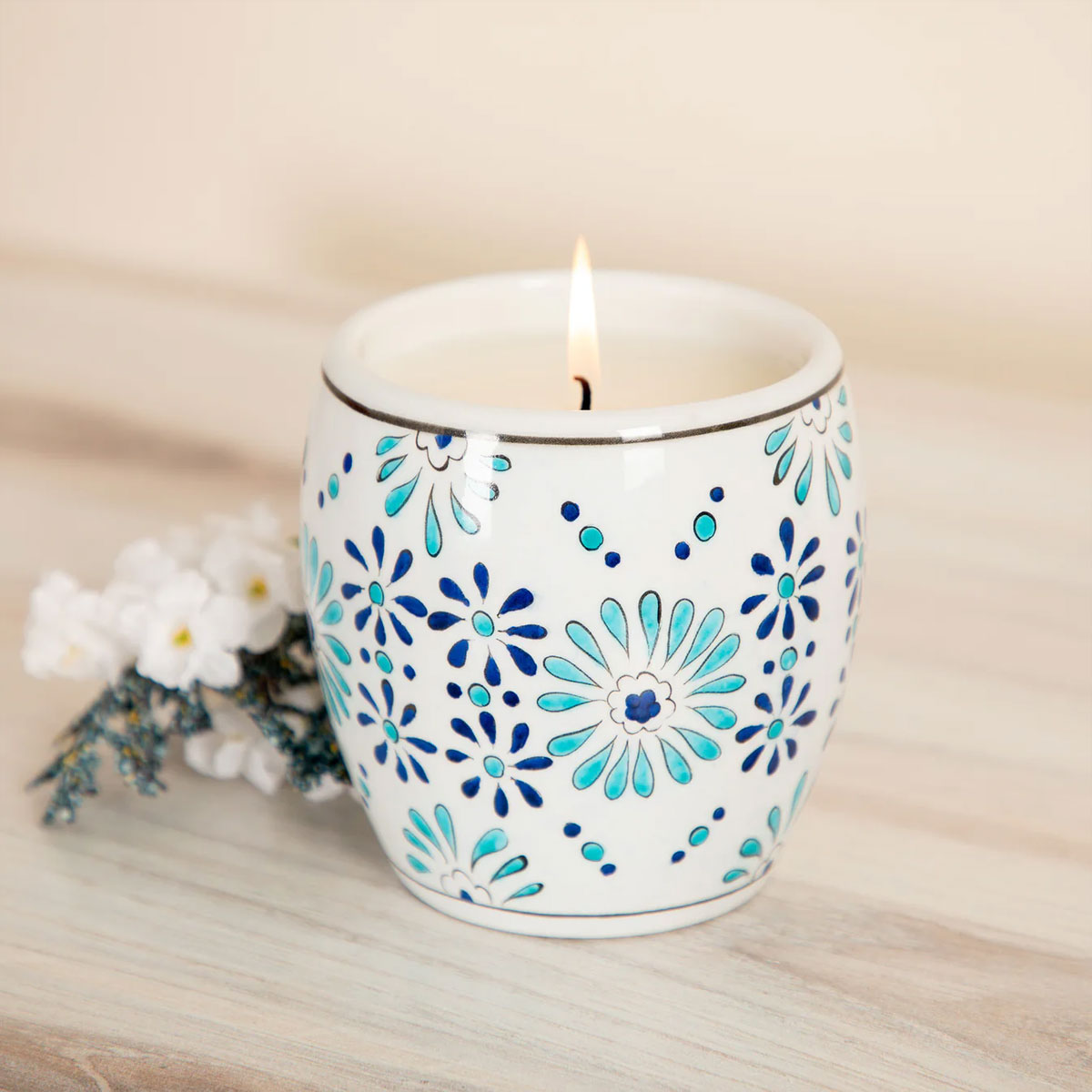 Candle in a decorative white holder with blue floral patterns on a wooden surface.