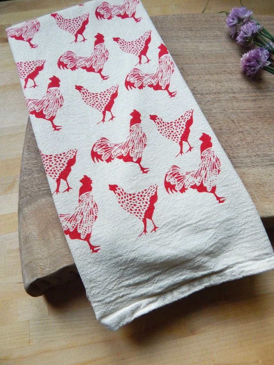 A hand-printed organic cotton towel, features a repeating pattern of red roosters and hens.