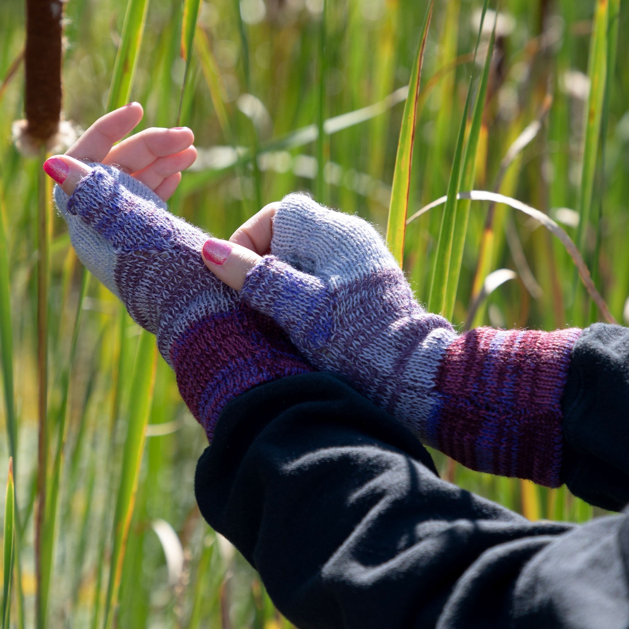 Hands wearing handmade alpaca fingerless mittens in a purple-toned color combination. Soft, hypoallergenic, and crafted in Bolivia.