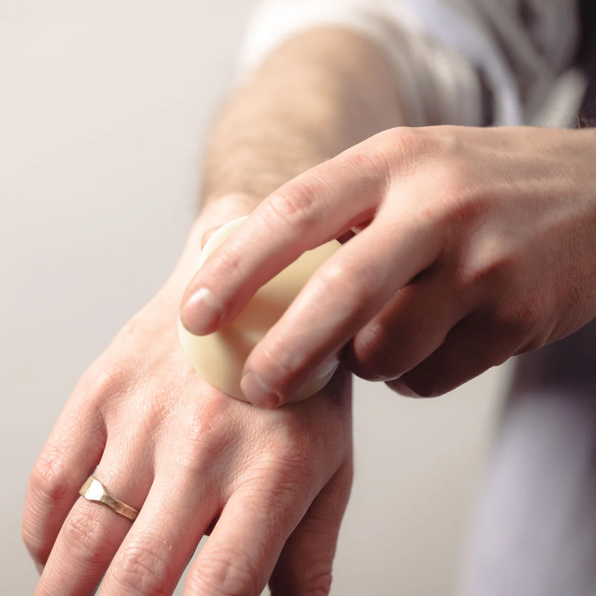 Person applying a small amount of Deep-Hydration Cocoa Butter Lotion Bar to their hand against a neutral background