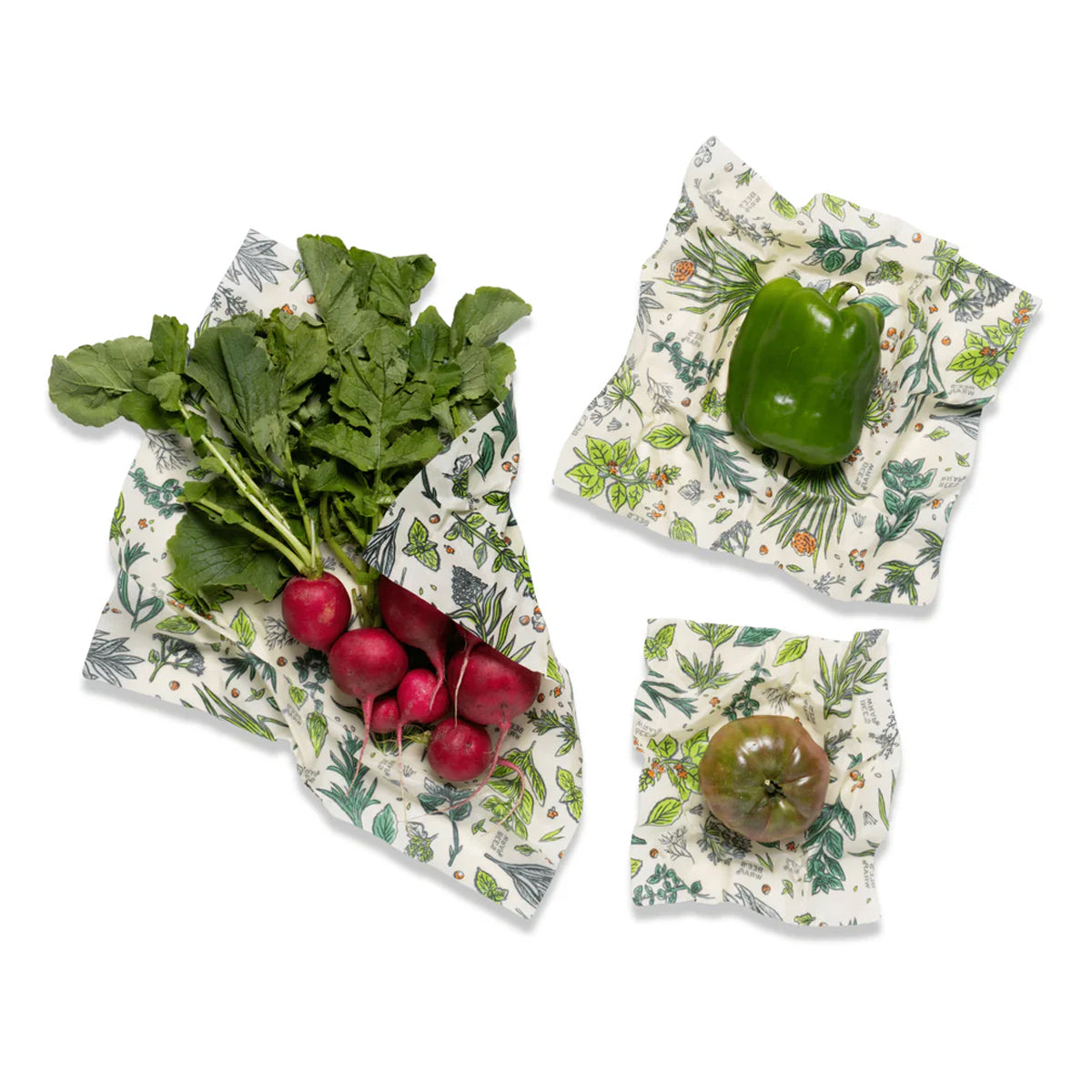 Three reusable beeswax  wraps with a green botanical leaf pattern are shown on a white background, each holding a fresh vegetables: radishes with greens, a green bell pepper, and a green tomato.