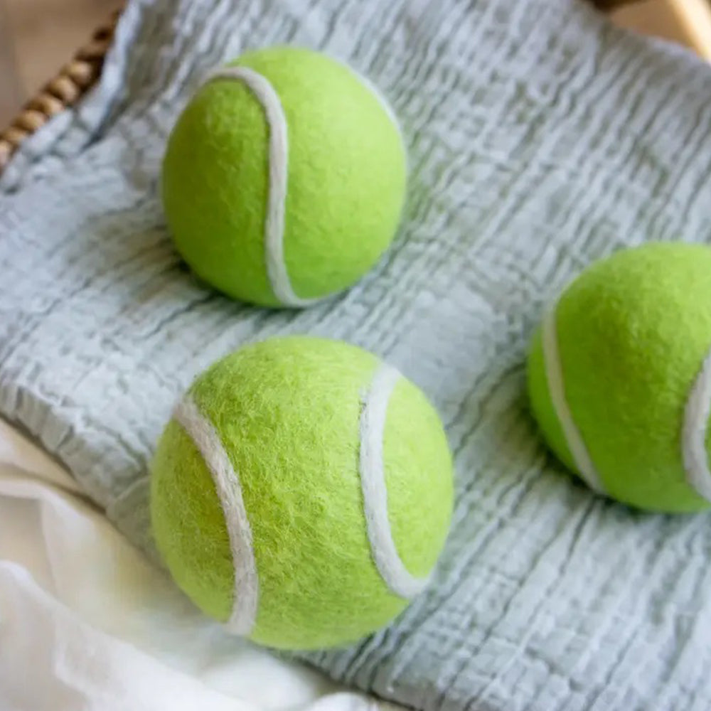 Three green wool eco tennis balls with white strings on a textured fabric surface.