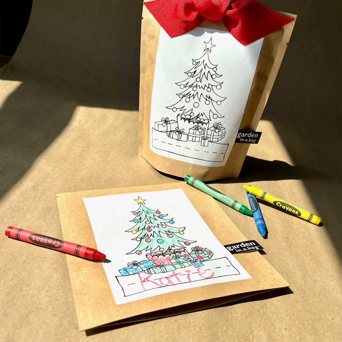 A "garden in a bag" Christmas-themed kit is shown, featuring a brown paper pouch with a red bow and a coloring page of a decorated tree and a dashed line for whom this is gifted