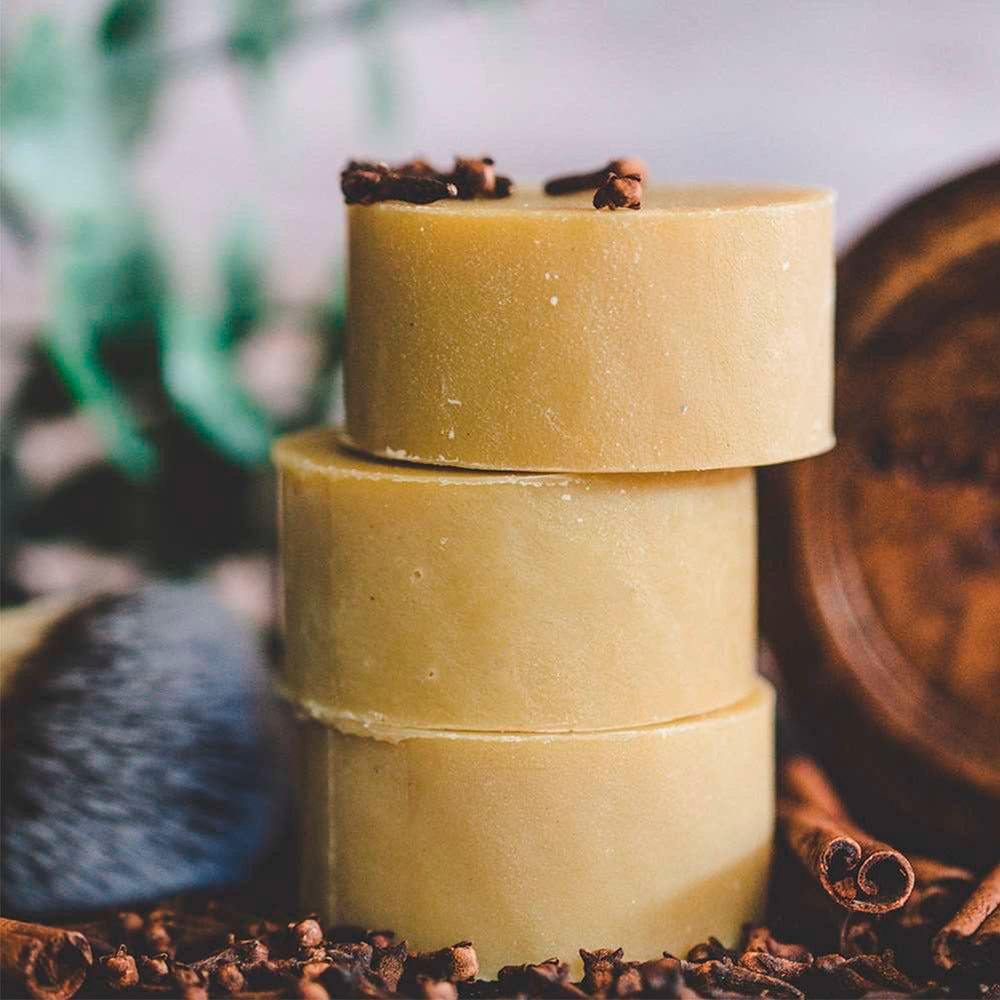 Stack of three cylindrical yellowish-beige bars of soap with cinnamon sticks on a blurred natural background