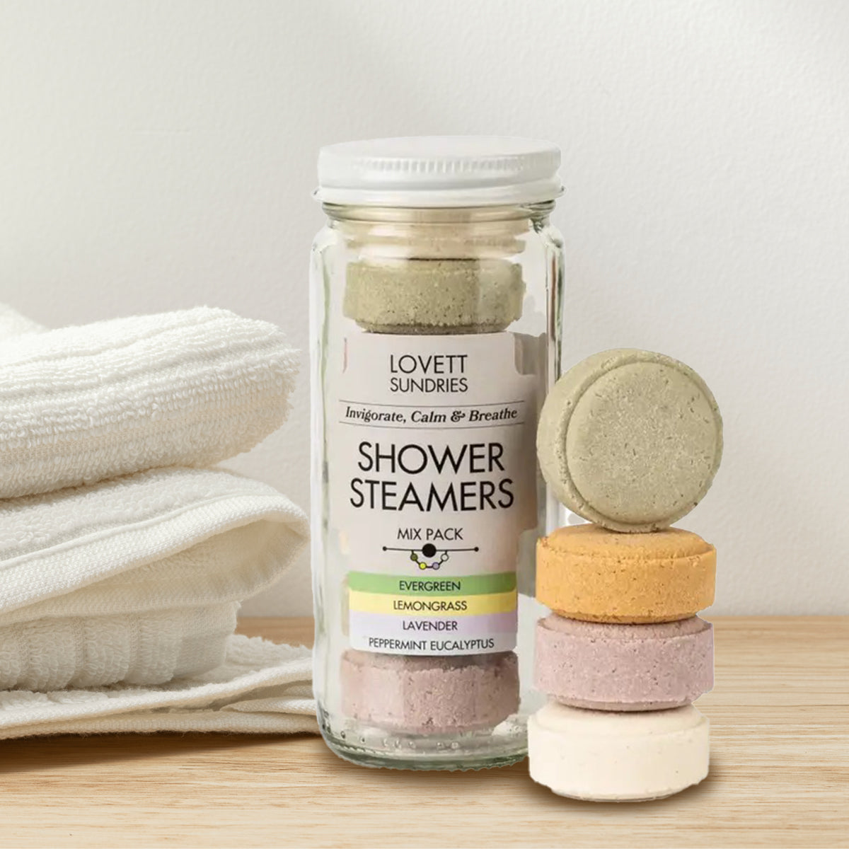 Jar of Lovett Sundries shower steamers with three stacked steamers on a wooden surface.