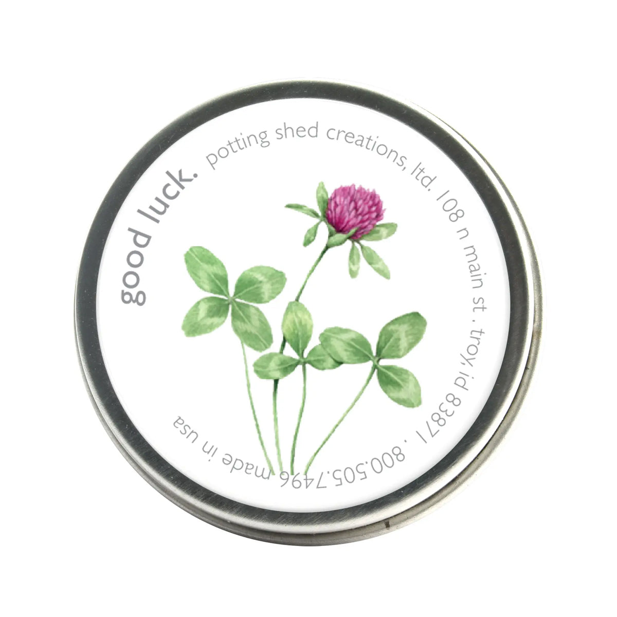 A silver tin of garden sprinkles with a white label on the lid. The label features a watercolor illustration of a four-leaf clover and a pink clover flower, with the text 'good luck, potting shed creations' around the edge.