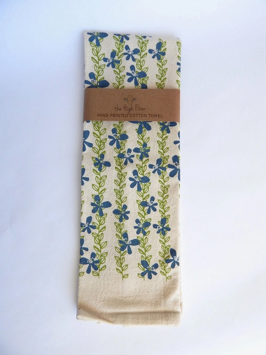 A charming organic cotton tea towel from 'the High Fiber,' featuring a hand-printed pattern of blue flowers and green leaves