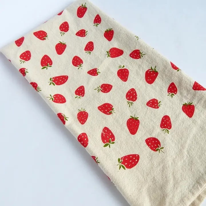 A white hand-printed organic cotton towel covered in a playful pattern of red strawberries and tiny green leaves.