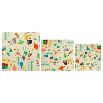 Three reusable beeswax wraps in varying sizes with a colorful forest animal and tree pattern, laid out flat and empty against a white background.