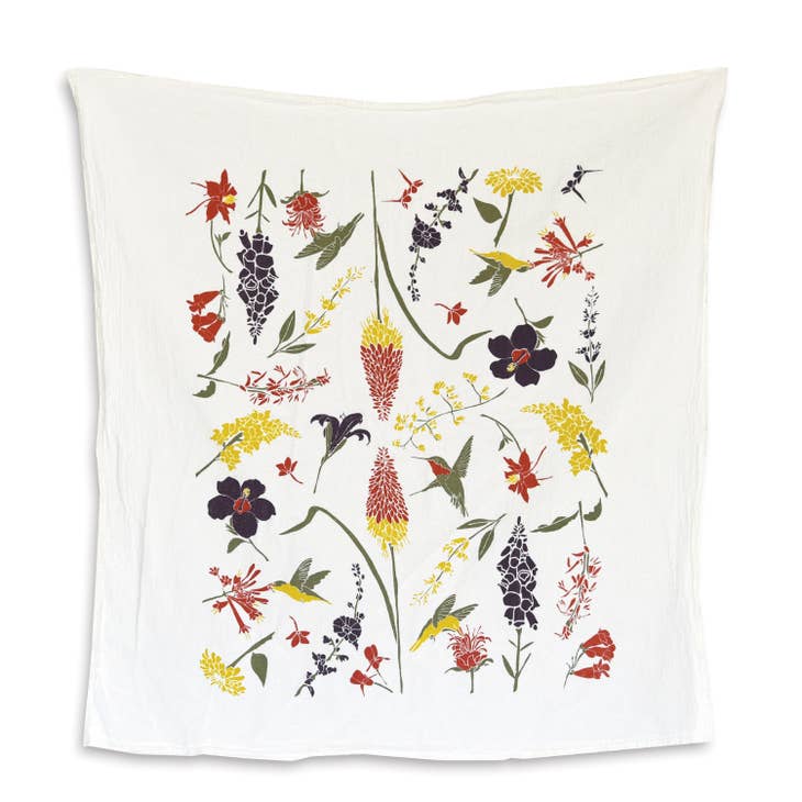 A white kitchen towel features a lively pattern of hummingbirds and flowers in shades of red, yellow, deep purple and green.